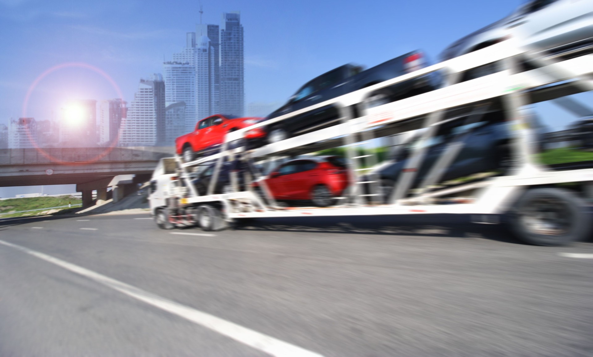 Trailer transports cars on highway with big city background