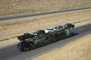 A large truck delivers new cars via highway.